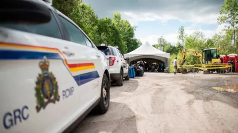 Getty Images RCMP cars parked at Roxham Road as construction workers install a new light pole in the distance.