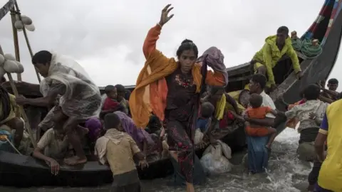 Getty Images Rohingya refugees jump from a boat as it begins to tip over after travelling from Myanmar to Dakhinpara, Bangladesh (12 September 2017)