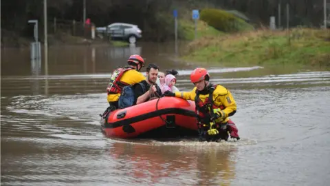 PA Wire A family in a boat is helped by emergency workers in Nantgarw, Wales