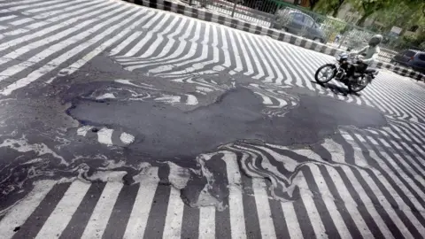 EPA A man in India rides a bike along a melted road