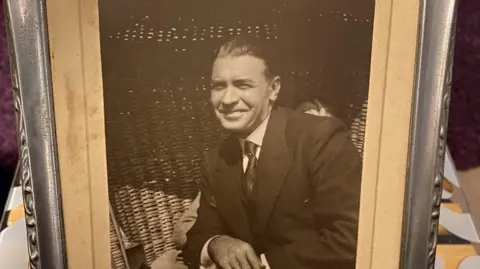 Family handout A black and white picture of Alan Kelly's father in a silver frame. He has dark hair combed back and is wearing a suit and tie and smiling.