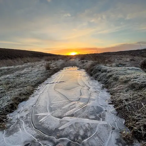 Viktoria Wilson The sun rises over a frozen field with a frozen stretch of water down the middle