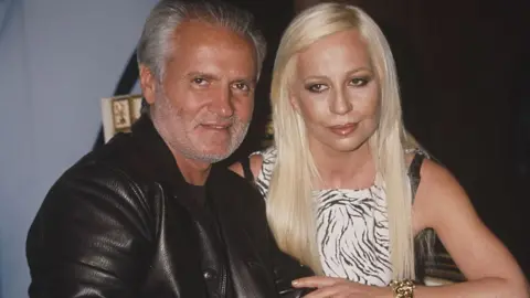 Getty Images Gianni and Donatella Versace at the launch for their new fragrance in 1996 - Gianni is dressed in all black leather and Donatella is wearing zebra print.