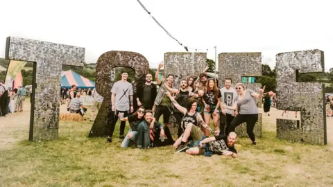 Gareth Bull A group of people posing in front of a big silver, glittery 'Trees' sign