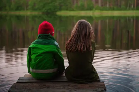 Getty Images A boy and girl sit on a pier