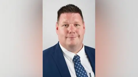 Gloucestershire County Council Nick Housden wearing a blue suit and blue tie with spots on it