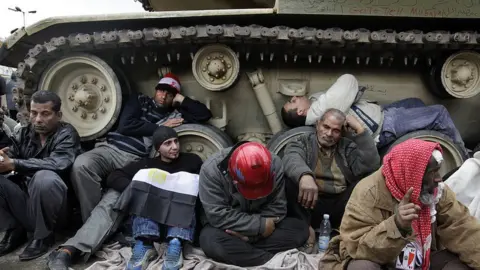 Getty Images Protesters huddle beside the tracks of a tank in Cairo (06/02/11)