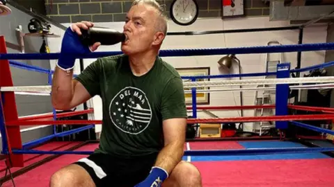 Huw Edwards / Instagram  Huw Edwards drinking water outside a boxing ring