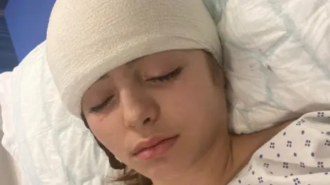 Olive Olive wears a bandage lying in a hospital bed