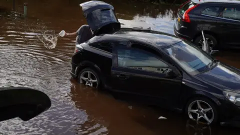 PA Media Resident in Rothbury in Northumberland bails water from their vehicle after the River Coquet burst its banks