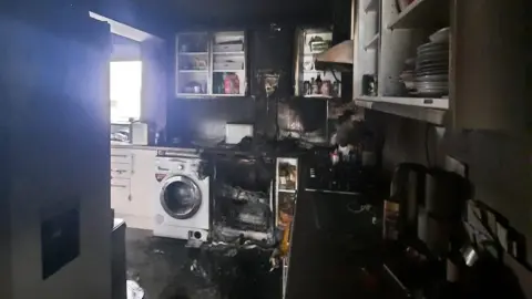 Essex Fire and Rescue Service A kitchen is blackened with smoke damage and a dishwasher is showing damage with no door.