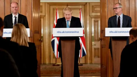 Getty Images Chief Medical Officer Professor Chris Whitty (L) and Chief Scientific Adviser Patrick Vallance (R) look on as British Prime Minister Boris Johnson (C) speaks during a coronavirus news conference inside number 10 Downing Street on March 19, 2020 in London