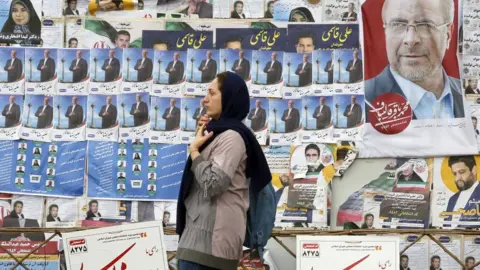 EPA File photo showing a woman walking past electoral posters in Tehran, Iran (28 February 2024)