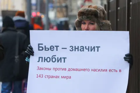 Getty Images A demonstrator pickets the Russian parliament quoting the saying, "If he beats you it means he loves you" - underneath the placard points out that 143 countries have a law on domestic violence