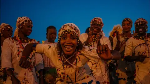 AFP Women dancing dressed in white with beaded head dresses. The woman in the middle is dancing and smiling