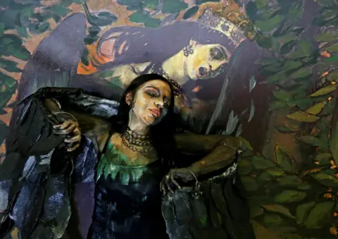 Ilya Naymushin / Reuters Model Alyona Alekseitseva presents a body of artwork by Russian artist Maria Gasanova, in Krasnoyarsk, Russia. Behind is a reproduction of Victor Vasnetsov's Sirin and Alkonost: A Song of Joy and Sorrow. 24 October, 2018