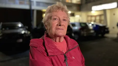 A woman in a red coat sitting outside a building at night