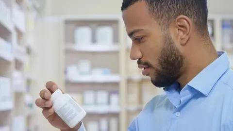 Getty Images A man looking at a pill bottle in a pharmacy