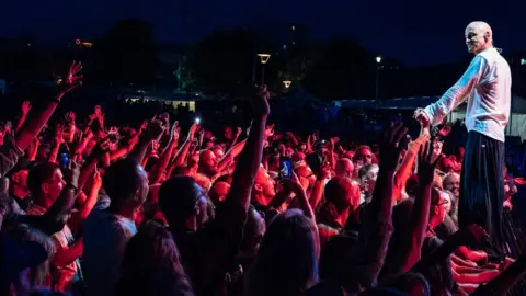 Ania Shrimpton James singer Tim Booth stands on the fence holding hands with audience members