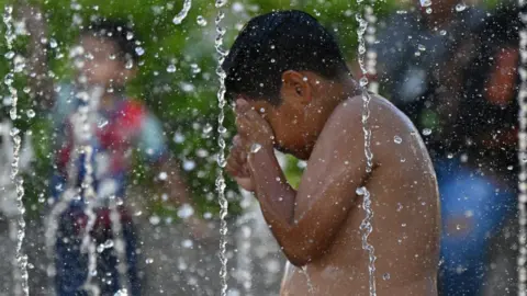 Getty Images A boy cools off in the waters of a fountain during hot weather in San Salvador.