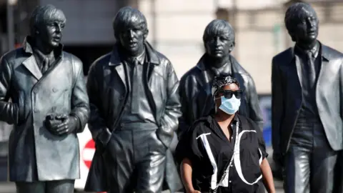 Reuters Woman with face mask walks in front of The Beatles statue on Liverpool waterfront