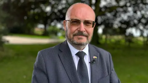 Andrew Turner/BBC Councillor Graham Plant standing in an area of woodland or park