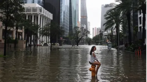 Getty Images Woman sat on fire hydrant in flooded Downtown Miami