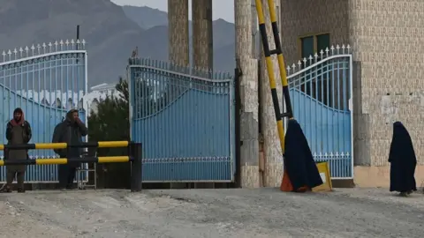 Getty Images Women wearing a burqa walk toward the main gate of Laghman University as Taliban fighters stand guard in Mihtarlam, Laghman province