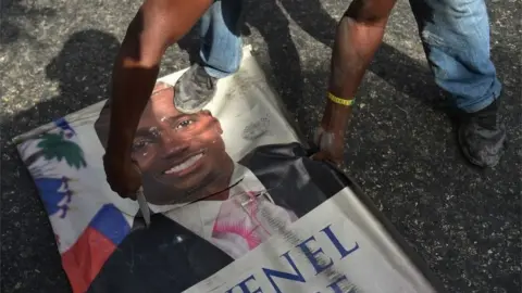 AFP Protesters destroy a poster of Haitian President Jovenel Moise as they demonstrate in the Port-au-Prince suburb of Petion-Ville on July 7, 2018, against a hike in fuel prices.