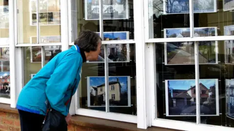 BBC Woman peering into estate agents window