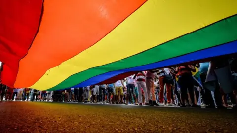 AFP A camera shot taken from beneath a large LGBT rainbow flag shows people's legs standing to the right of the flag
