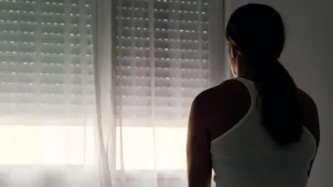 Getty Images Rear view of an unrecognizable abused woman sitting on her bed looking out the window