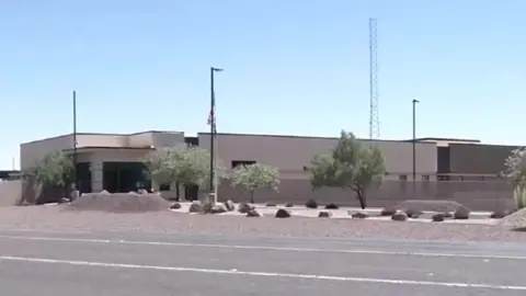 EVN A grey, low building sits on a nondescript highway under a hot sun in this photo