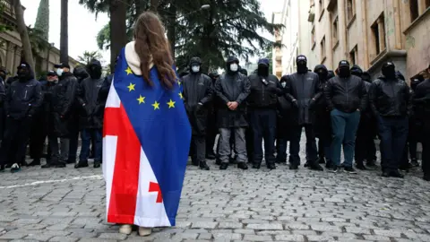 A protester wearing a Georgian and European flag faces off policemen blocking a street during a protest