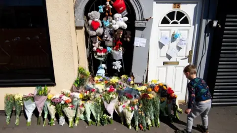 PA Media Boy lays a flower at the scene