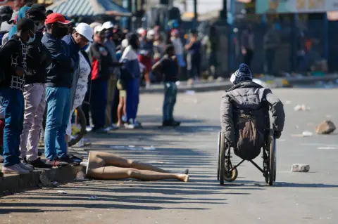 AFP People look at a man in a wheelchair as he moves past the looted and vandalised Lotsoho Mall in Katlehong township, East of Johannesburg, on 12 July 2021