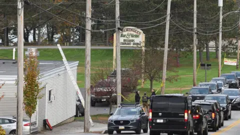 Reuters Stopped cars, Schemengees sign, white building, green grass.