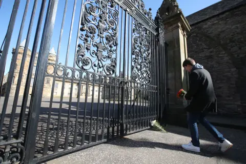 PA Media A well-wisher lays a floral tribute at the gates of The Palace of Holyroodhouse in Edinburgh, Scotland