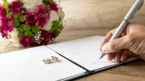 Gajus/Getty Images Man signing a marriage register