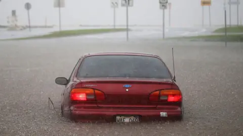 Getty Images A car is stuck partially submerged in floodwaters from Hurricane Lane rainfall on the Big Island, Hawaii, 23 August 2018