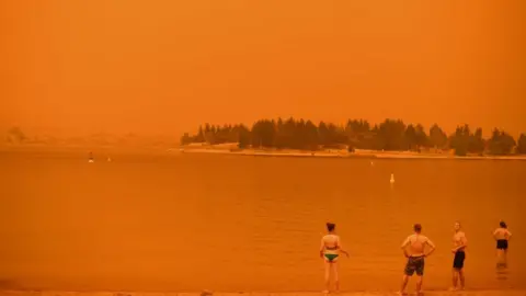 Getty Images Swimmers stand near the water under a red sky at Jindabyne in New South Wales on 4 January