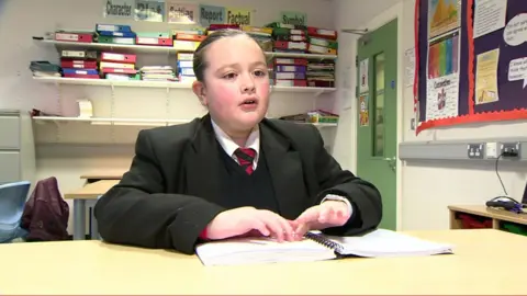 Eryn Kirkpatrick sitting at a desk wearing school uniform reading braille