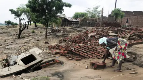 EPA A woman looks for her belongings, after the Tropical Storm Ana hit the district of Tete, Mozambique, 27 January 2022.