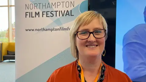 Woman with medium-length blonde hair standing in front of Northampton Film Festival sign