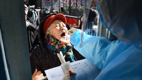 Getty Images This photo taken on January 6, 2021 shows a medical worker taking a swab sample from a woman outside a residential compound following a new outbreak of the Covid-19 coronavirus in Shijiazhuang