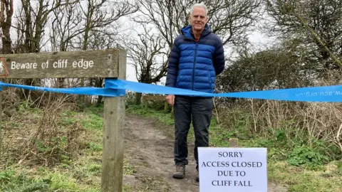 GUY CAMPBELL/ BBC Geoff Abell standing behind the cordoned-off area of the footpath