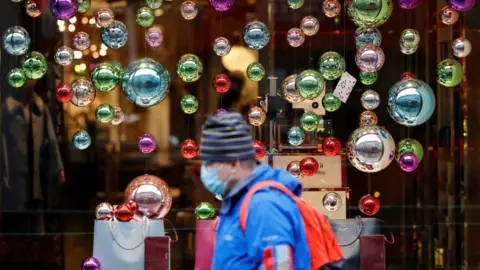 Getty Images A man wearing a mask walks past a Christmas display