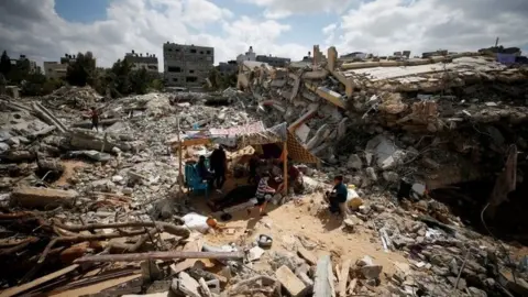 Reuters Palestinians sit in a makeshift tent amid the rubble of buildings destroyed in Israeli air strikes in Gaza (23 May 2021)