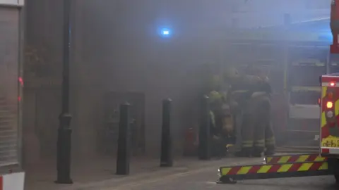 PA Media Firefighters enclosed in smoke from the fire at the Admiralty pbu