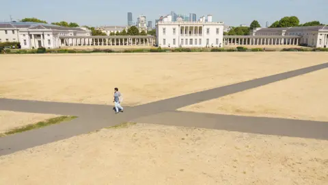 PA Media A woman walks on a path at Greenwich Park